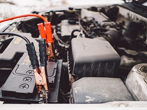 Car battery under the hood with jumper cables