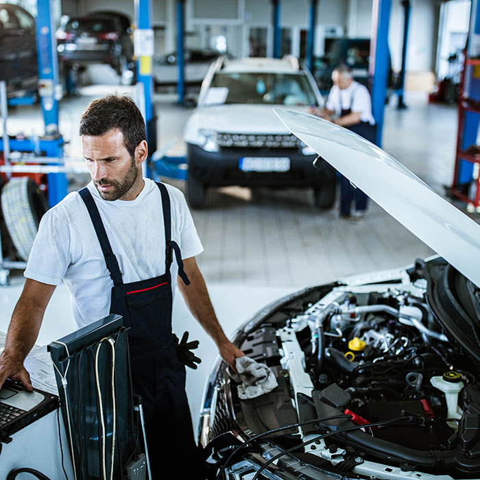 Car mechanic using computer while working on car diagnostics in a repair shop