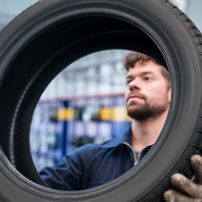 Young apprentice holding car wheel in the auto repair shop