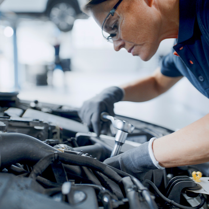 Female mechanic with socket wrench working on car engine in auto repair shop