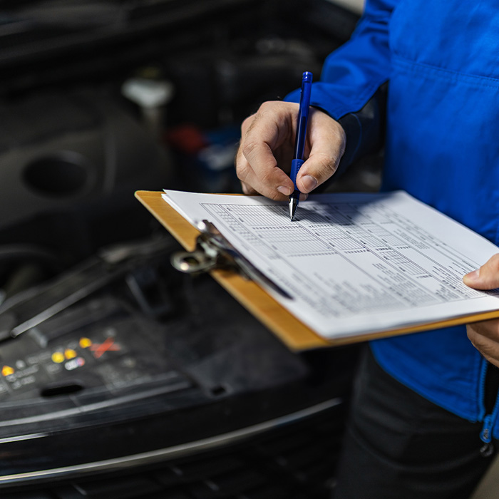 A mechanic inspects a vehicle engine while checking a maintenance checklist in a workshop