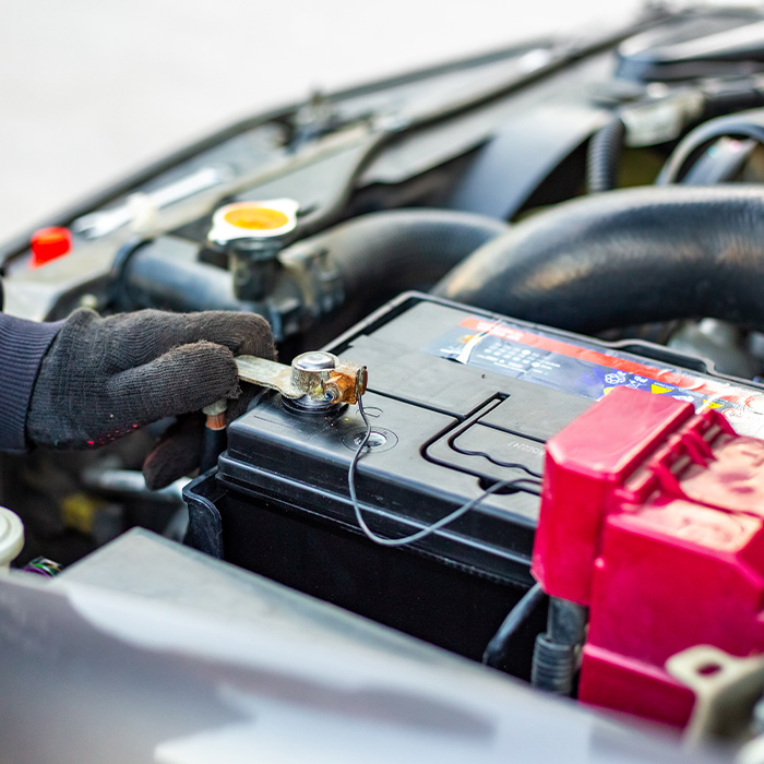 Mechanic wearing gloves loosens a car battery terminal with a wrench under the open hood of a vehicle