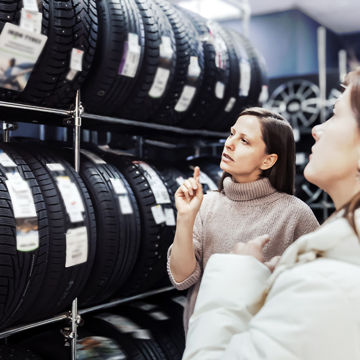 woman thoughtfully examines available tires displayed on shelves while seller provides guidance